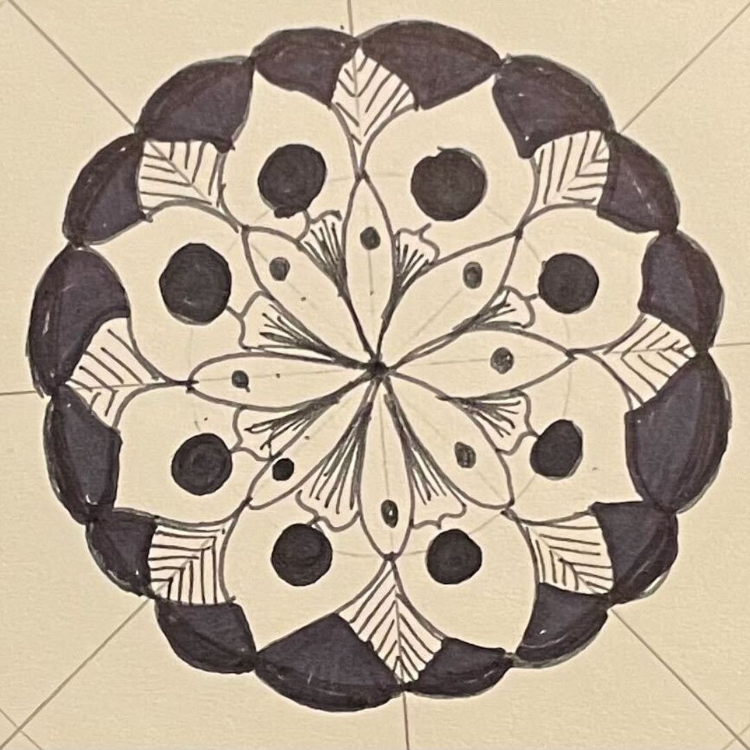 The image shows a hand-drawn mandala with intricate leaf and petal-like patterns creating a harmonious circular design. The mandala is primarily in black ink with shaded areas to add depth, and it is drawn on a square piece of paper with a neutral background. The symmetrical design and detailed artwork make it visually appealing.