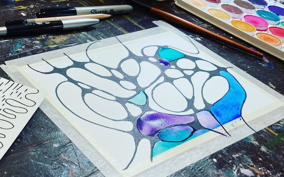 (Brain Doodles artwork by Angie Ebba): A piece of Brain Doodles artwork by artist Angie Ebba sits taped to a work surface. Black organic lines form a web of irregular, interconnected shapes, some filled with bright watercolor washes in blue, turquoise, purple, and pink. Surrounding the piece are art tools—a Sharpie, pencil, pen, paintbrush, and a watercolor palette—along with a small reference sketch showing similar linework, capturing the creative process behind the piece.