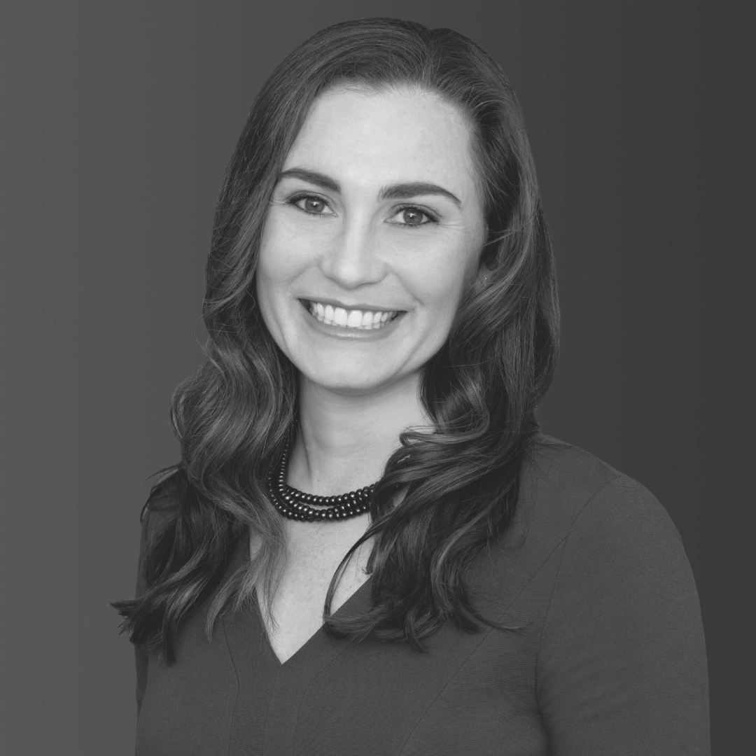 Mission Belonging board member Jillian Danback-McGhan, smiling in a dark top and beaded necklace, with long wavy hair against a soft gradient background.