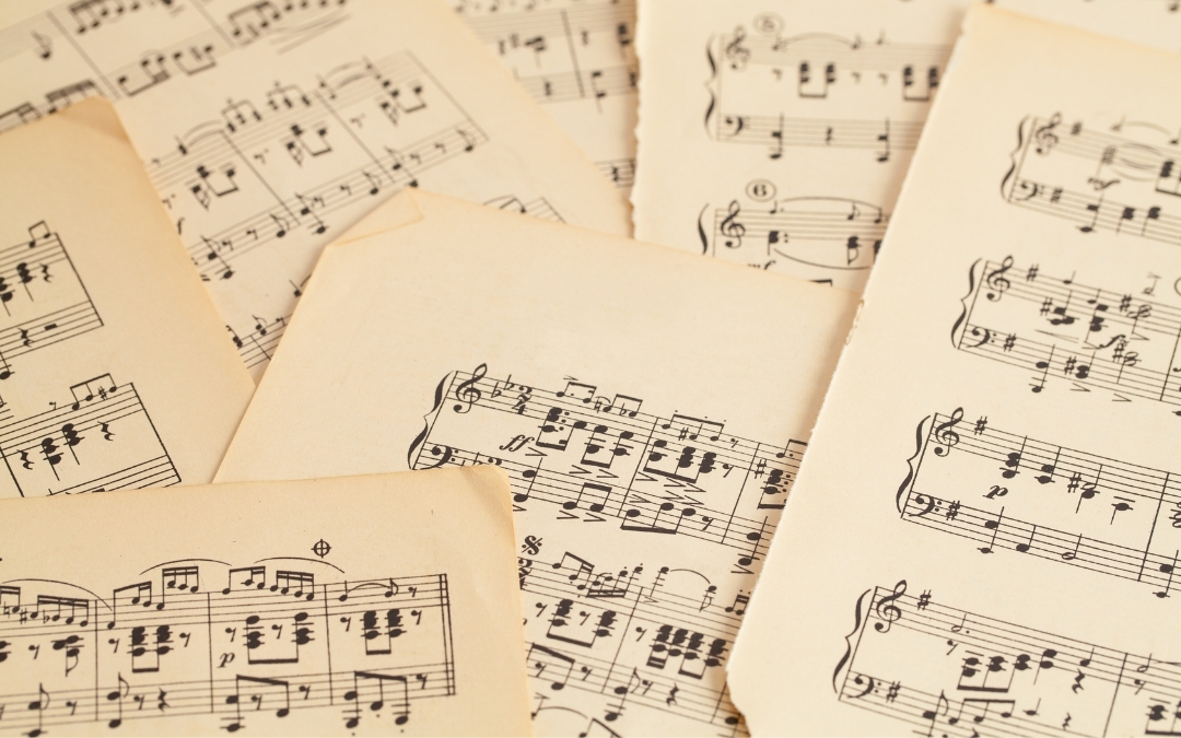Music — Creative Expression Workshop Several sheets of aged music notation lie scattered on a surface, showing staffs, notes, rests, and musical symbols on yellowed paper with worn edges.