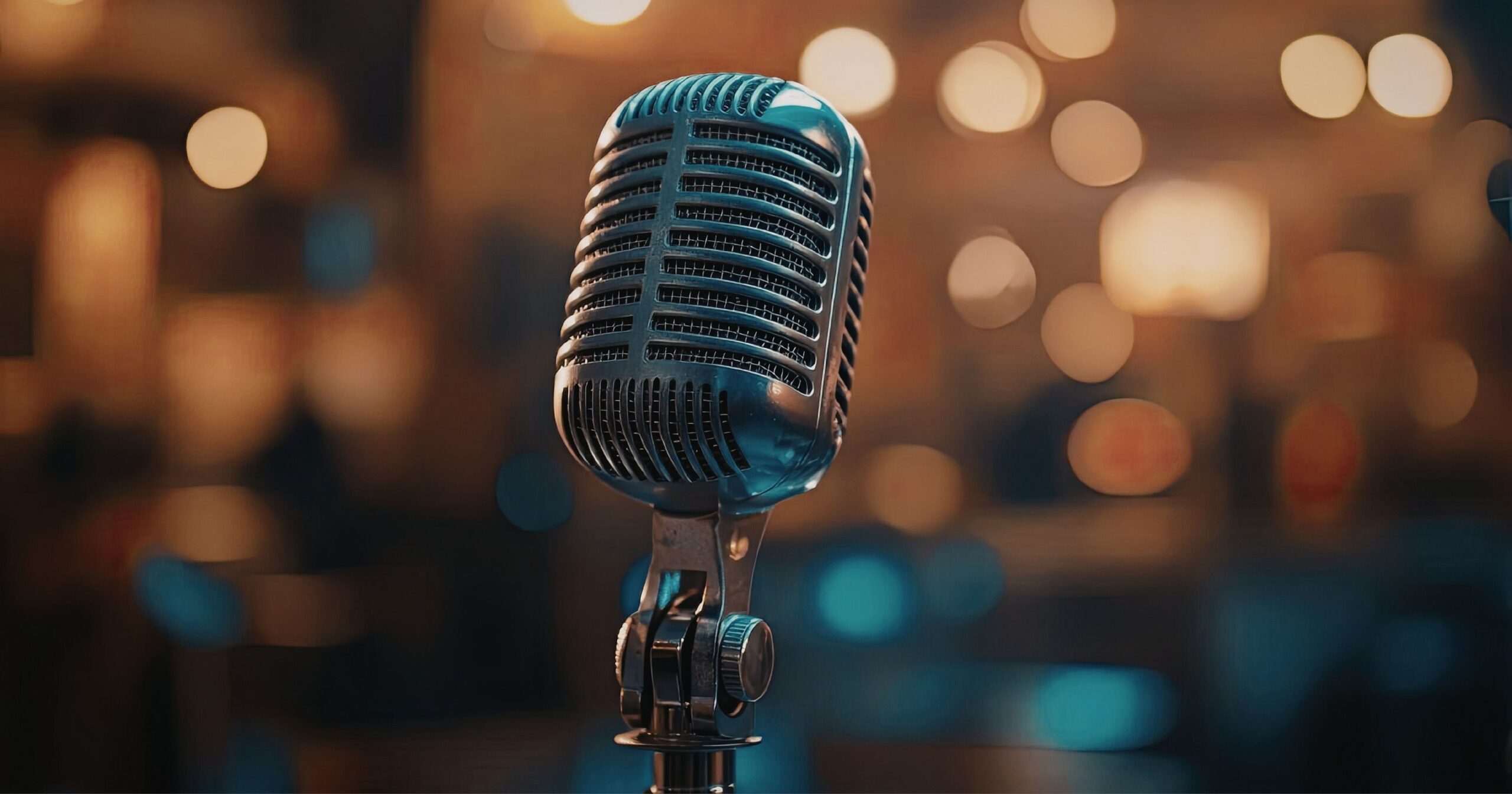 A close‑up of a vintage‑style microphone on a stand with warm blurred lights in the background.