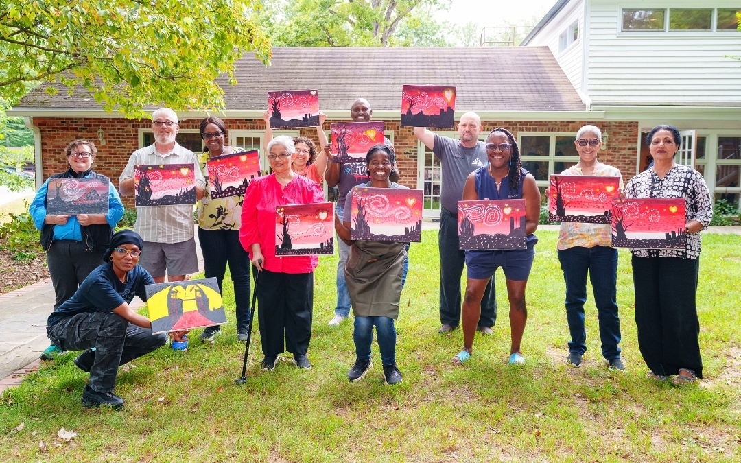 Participants at Day of Belonging 2026 at Rockwood Manor on September 19 hold up paintings created during Natasha Lewis’s painting activity; photo by Doug Sanford.